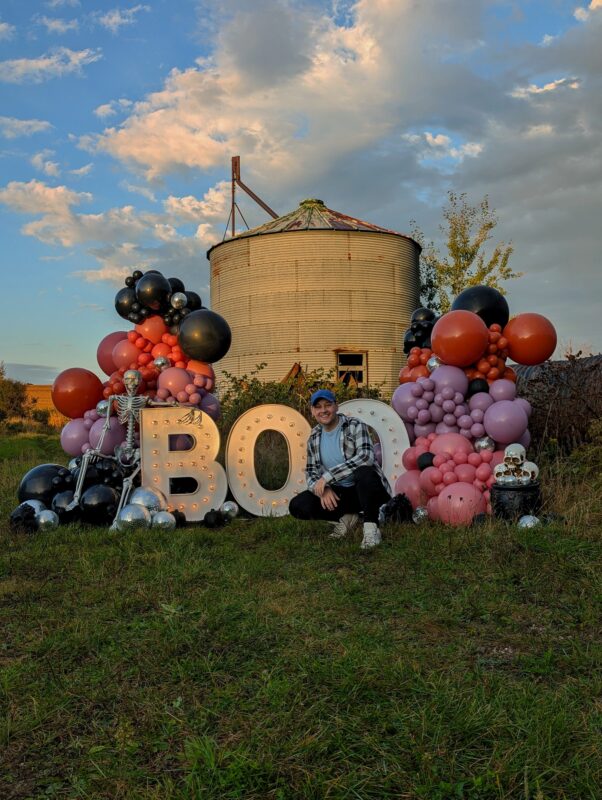 Pawel Rzeznik beside a large autumn balloon display with pumpkins and oversized BOO letters.