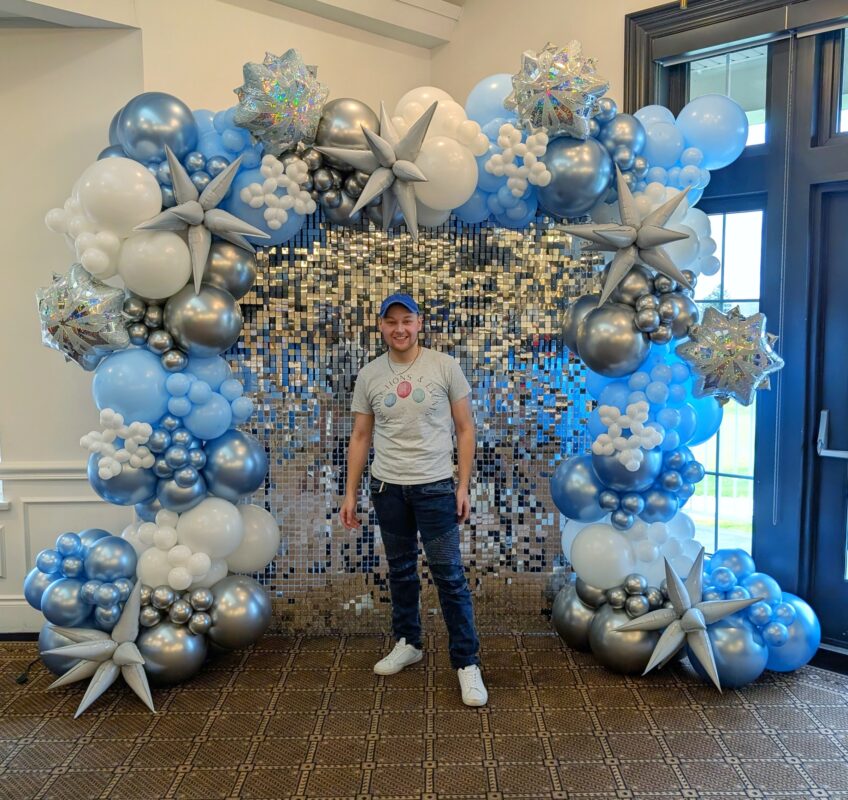 Pawel Rzeznik in front of a detailed blue, white and silver balloon installation.