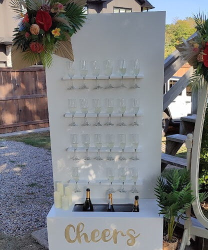 Champagne wall with a custom 'Cheers' decal, glasses, and floral decoration.