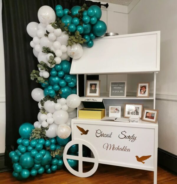 Elegant dessert cart with turquoise and white balloons, eucalyptus, and photo frames.