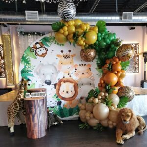 Jungle-themed first birthday backdrop with cartoon animals, balloons, and 'MR. ONEDERFUL' sign.