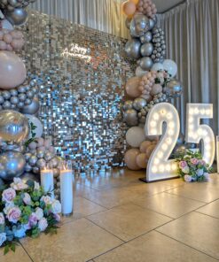 Silver shimmer wall backdrop rental in Kitchener Waterloo with blush, white, and chrome balloon garlands, marquee numbers 25, florals, and candles for an elegant anniversary event.
