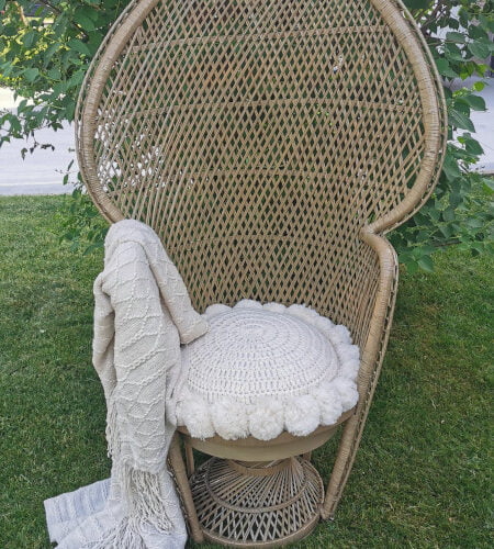 Peacock wicker chair with a white cushion and throw.