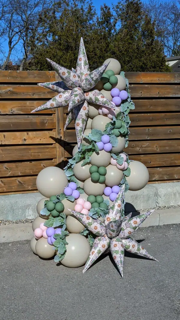 Colorful balloon decoration featuring floral star shapes and various pastel-colored balloons against a wooden backdrop. Perfect for events.