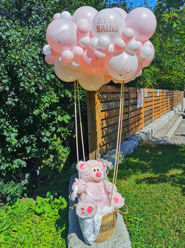 A pink and white balloon arrangement forming a cloud over a pink teady bear.