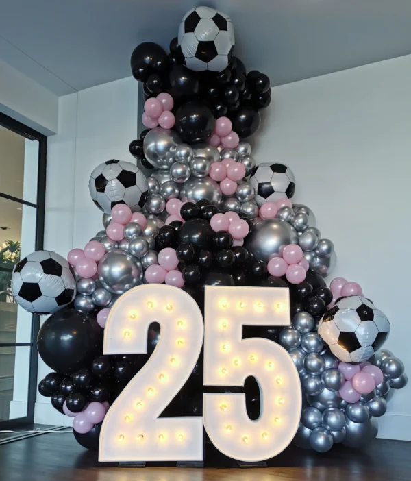 Black and white balloon column with soccer ball foil balloons behind "25" marquee letters.