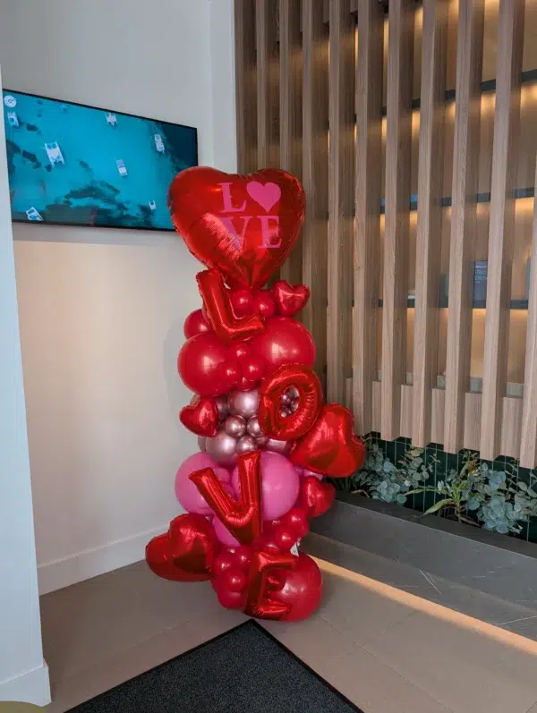 Colorful heart-shaped balloons spell "LOVE," creating a festive display in a modern indoor setting.