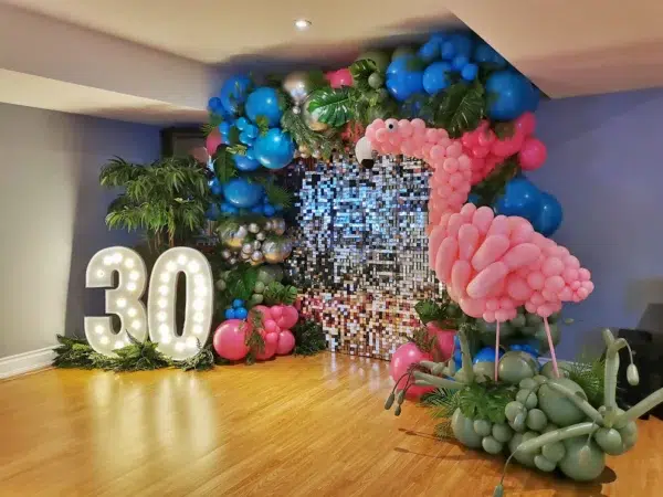 Colorful party decorations featuring a large illuminated "30," a pink flamingo balloon, and vibrant balloon arrangements.