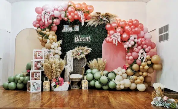 Colorful balloon decor featuring pink, green, and gold shades, with floral accents, for a cheerful baby celebration backdrop.