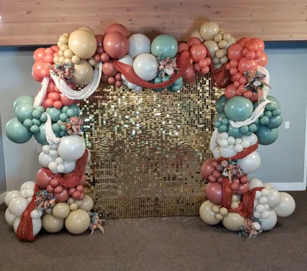 Colorful balloon arch with gold sequined backdrop, perfect for celebrations and photo opportunities. Floral accents add a charming touch.