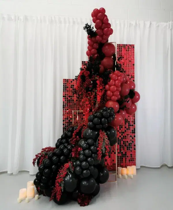 A vibrant display of black and red balloons, complemented by floral accents and candles, set against a white backdrop.