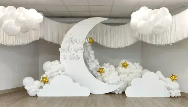 A whimsical event backdrop featuring a white crescent moon, fluffy clouds, and balloon accents with golden stars. Perfect for celebrations.