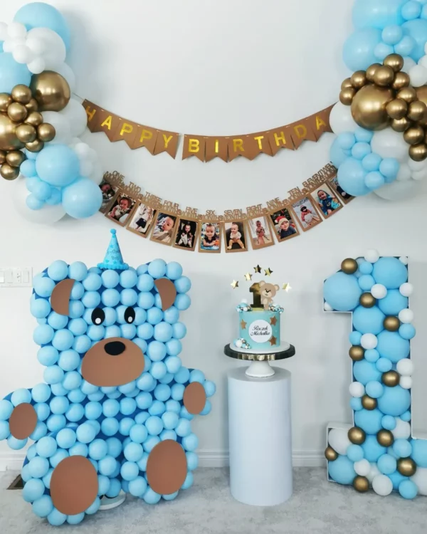 A colorful birthday setup featuring a blue balloon bear, a festive cake, a "Happy Birthday" banner, and photo memories.