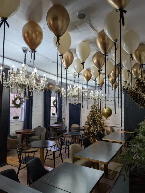 A stylish café decorated with gold and white balloons, elegant chandeliers, and a festive Christmas tree, creating a cozy atmosphere.