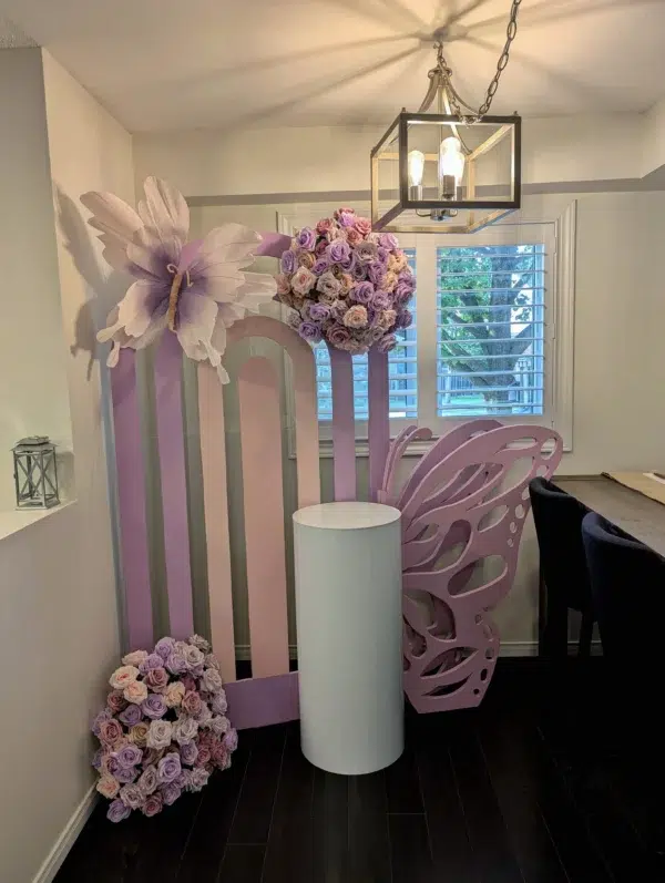 Purple and pastel floral backdrop with a butterfly, round pedestal, and elegant lighting in a cozy interior space.