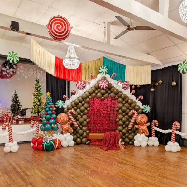 Festive gingerbread house display made of colorful balloons, featuring candy accents and a decorated Christmas tree, perfect for holiday celebrations.