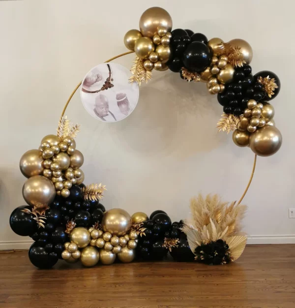 Elegant balloon arch featuring gold and black balloons, adorned with decorative foliage and a circular photo display. Perfect for celebrations.