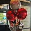 A foil balloon bouquet featuring a large custom decal balloon, metallic red orb balloons, and silver star balloons.