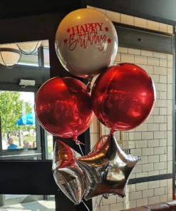 A foil balloon bouquet featuring a large custom decal balloon, metallic red orb balloons, and silver star balloons.