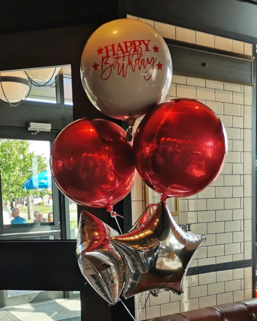 A foil balloon bouquet featuring a large custom decal balloon, metallic red orb balloons, and silver star balloons.