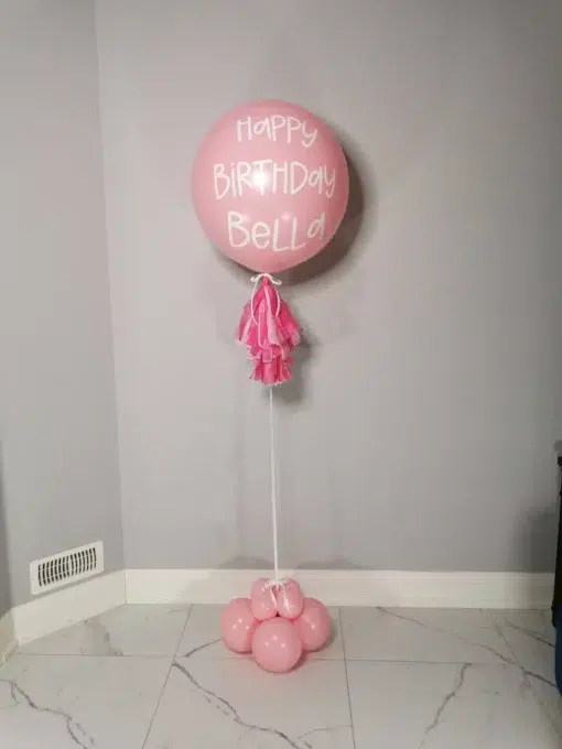 A large pink 24-inch helium balloon with a custom message, featuring a tassel tail and balloon base.