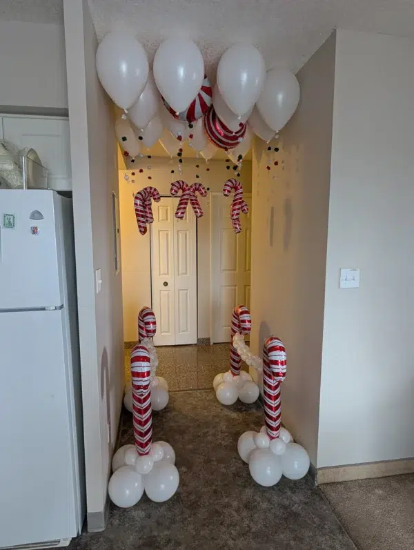 Entrance decorated with white and red balloons, candy cane-shaped inflatables, and festive ornaments creating a joyful holiday atmosphere.