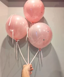 Three pink helium balloons with sparkling accents and ribbons, held together in a stylish bouquet