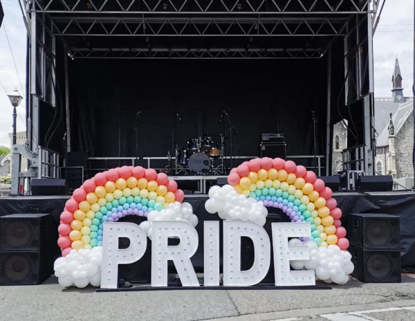 A stage decorated with colorful balloon rainbows and the word "PRIDE" in large illuminated letters, ready for a celebration.