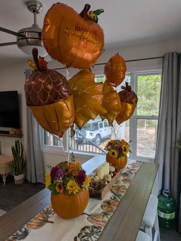 Thanksgiving-themed table decor featuring pumpkin balloons and floral arrangements in pumpkins, set in a cozy indoor space.