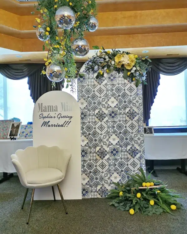 Festive wedding backdrop featuring a decorative wall, potted greenery, disco balls, and a white chair for guest seating.