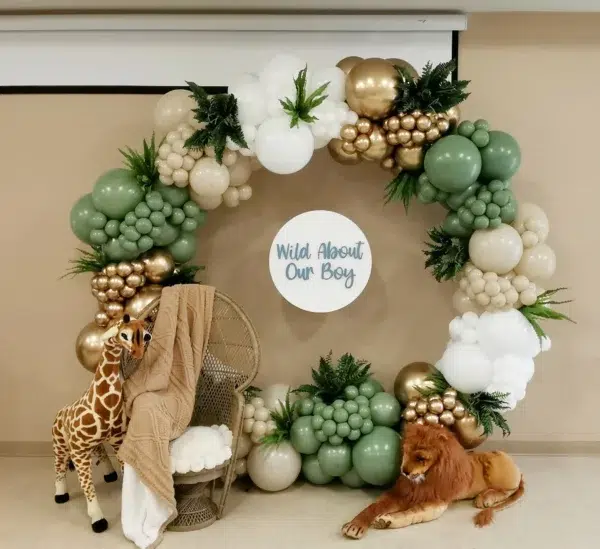 A decorative backdrop featuring green and gold balloons, a sign reading "Wild About Our Boy," and plush animals for a celebration.