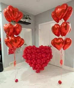 Two red heart-shaped balloon bouquets and a large red balloon heart sculpture displayed against a neutral backdrop