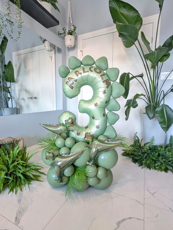 A dinosaur-themed balloon number stack featuring a bold single digit balloon, a fierce dinosaur accent, and a custom name decal.