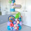 A vibrant balloon number stack featuring Stitch characters, tropical-themed floral balloon décor, customizable numbers, and personalized name decals.