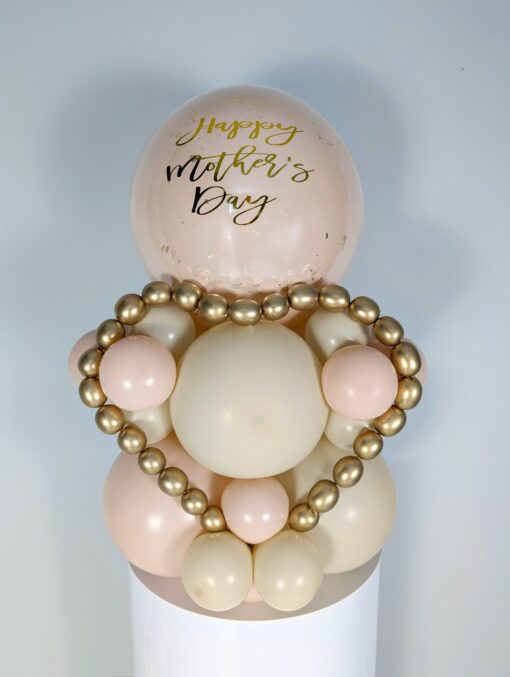 Balloon display with cream, blush, and gold balloons, metallic gold mini garland, and a personalized large balloon topper.