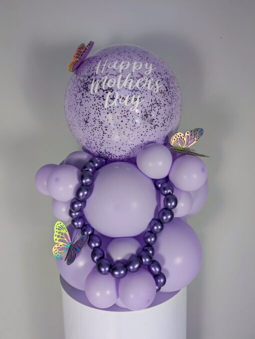 Lilac and lavender balloon display with large speckled balloon, metallic mini garland, and butterfly decorations.
