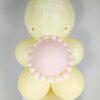 Pastel yellow and blush balloon display with daisy accents, a mini balloon garland, and a personalized large balloon topper.