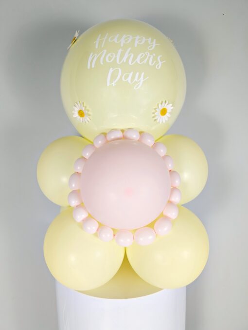 Pastel yellow and blush balloon display with daisy accents, a mini balloon garland, and a personalized large balloon topper.