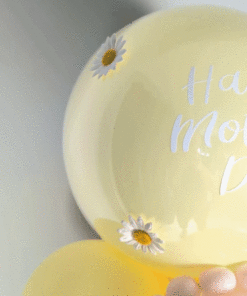 Pastel yellow and blush balloon display with daisy accents, a mini balloon garland, and a personalized large balloon topper.