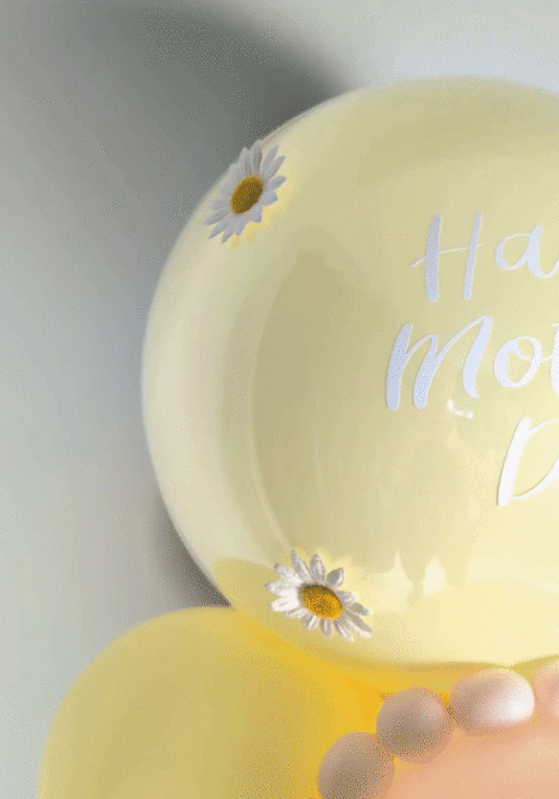 Pastel yellow and blush balloon display with daisy accents, a mini balloon garland, and a personalized large balloon topper.