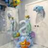 Under the Sea Splash Stack balloon number display with blue balloons, bubble accents, fish, dolphin, and starfish foil balloons for a birthday party.