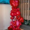 Organic Valentine’s balloon column featuring red and pink balloons with heart foil balloons and stacked LOVE letter balloons in a modern sculptural design.