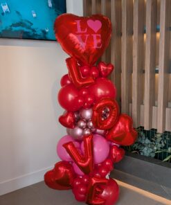 Organic Valentine’s balloon column featuring red and pink balloons with heart foil balloons and stacked LOVE letter balloons in a modern sculptural design.