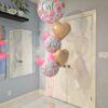 Pink “It’s a Girl” helium balloon bouquet with champagne heart foils and clear bubble balloons on a blush balloon weight base. 💕