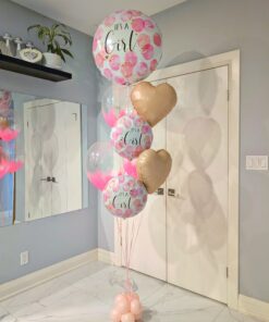 Pink “It’s a Girl” helium balloon bouquet with champagne heart foils and clear bubble balloons on a blush balloon weight base. 💕