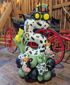 Farm themed balloon number stack with cow print balloon, tractor topper, corn balloons, and green organic balloon base for a barnyard birthday party.
