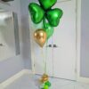 Emerald shamrock heart helium balloon bouquet with green and gold latex balloons and gold spiral base detail.