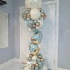 Pastel Easter balloon column with pearl white, blue, and gold balloons, featuring egg balloons and a “Happy Easter” topper.