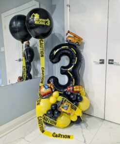 Construction themed balloon setup with black and yellow number stack, caution tape accents, helium bouquet, and personalized name decal
