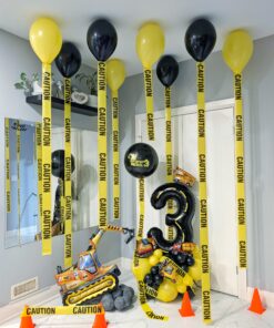 Construction themed balloon setup with number stack, ceiling helium balloons with caution tape tails, excavator balloon, pylons, and rock accents